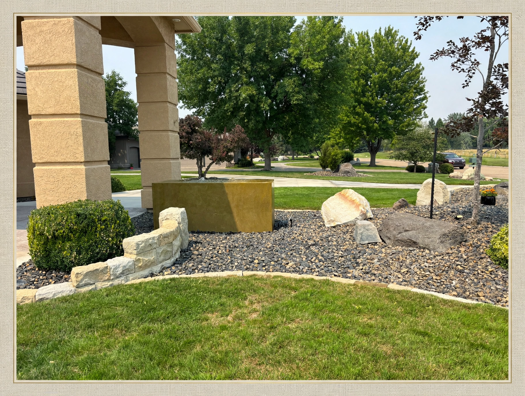 A hardscaped water feature with boulders, decorative gravel, and stone edging beside a stucco column